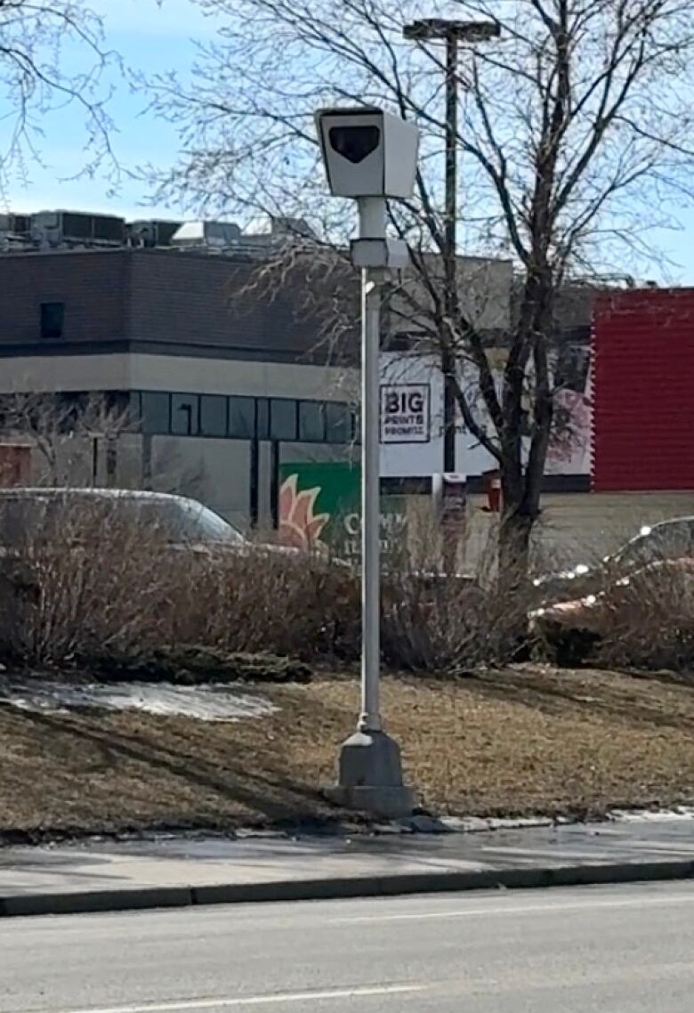 a white pole with a camera box on top of it sits next to a main road.