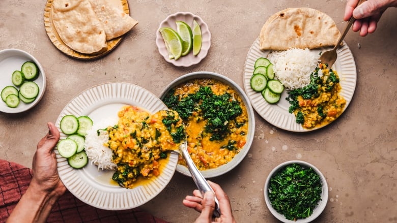 Overhead shot of hands adding a spoonful of dal with greens to a plate with rice on it. 