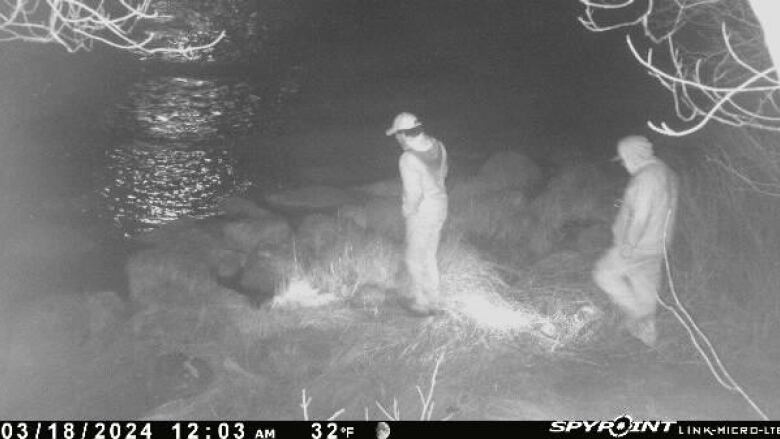 Night vision shot of two figures on a riverbank.