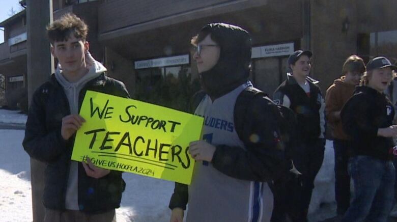 Two young boys are pictured holding a sign that says 'We support teachers. #GiveUsHoopla2024'