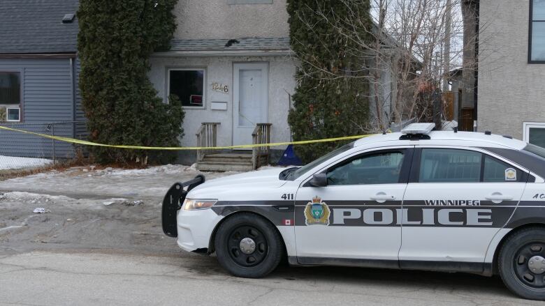 A police car is parked on the road in front of a 1 1/2-storey house, which is blocked by yellow police tape.