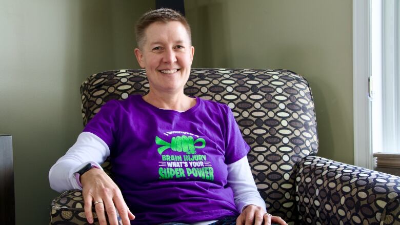 A middle-aged woman wearing a purple T-shirt that says, 'I survived a brain injury. What's your super power.'