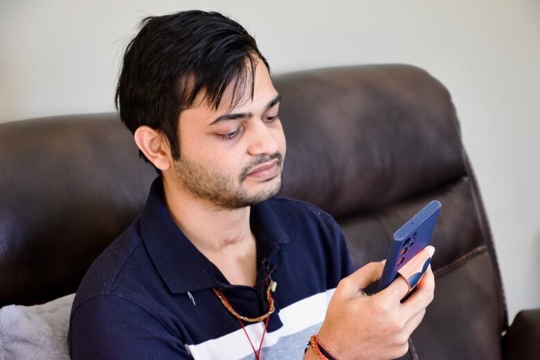 A young man sits on a couch looking at his cellphone.