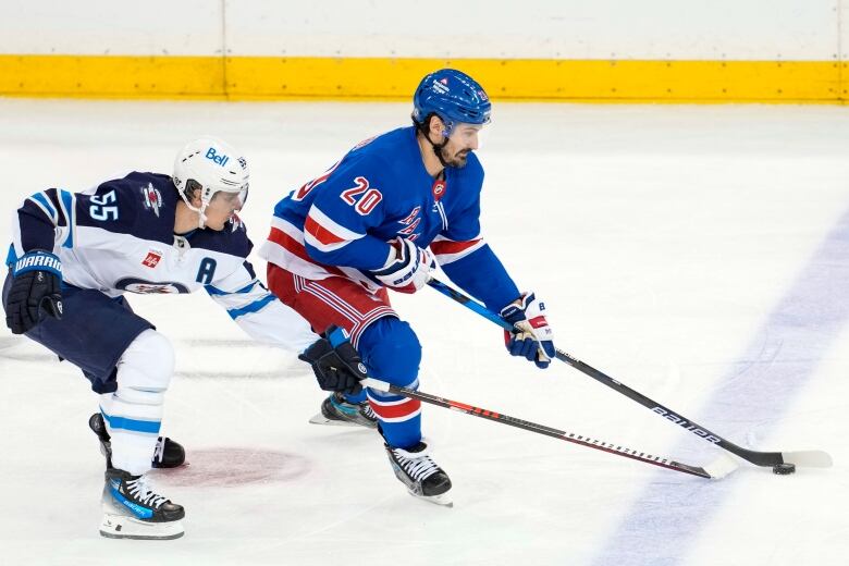 Two hockey players of opposite teams are seen battling for the puck on the ice.