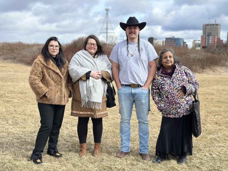 Four people stand in a line outside in a field of dead grass.