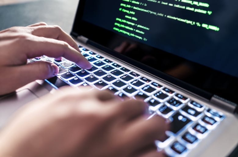 A closeup shows a person's hands typing on the keyboard of a laptop computer, with blurred green text on its screen.