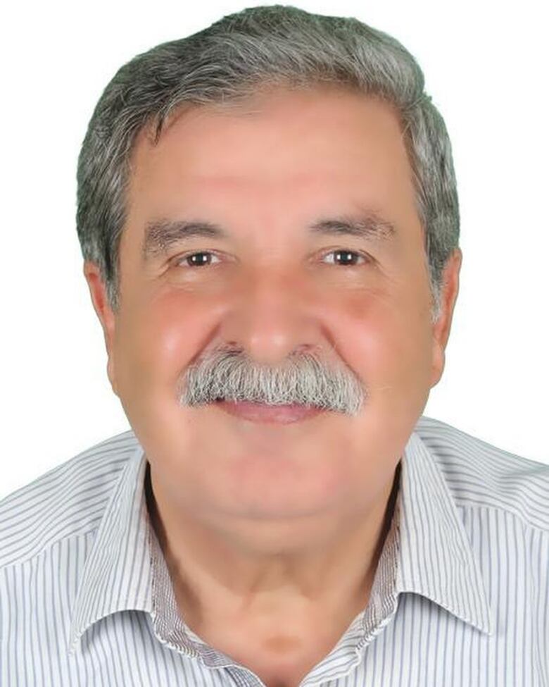 Close-up of a smiling elderly man with a gray mustache against a white background. 