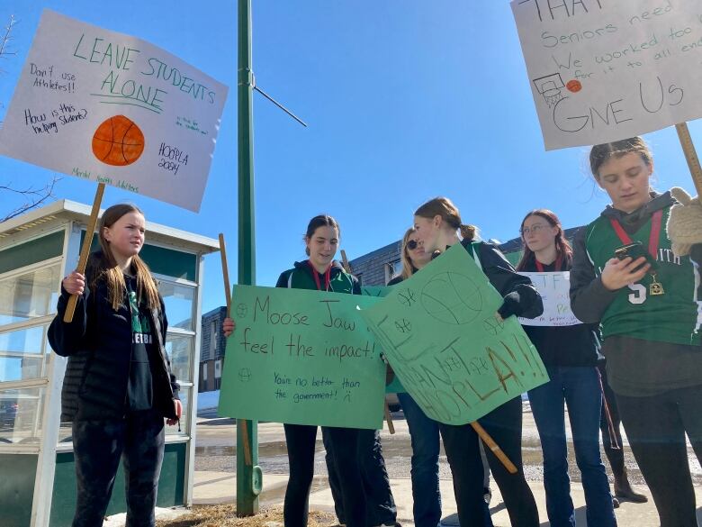 A group of high school aged girls hold protest signs.