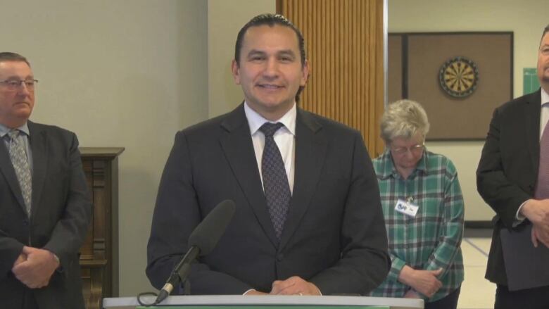 A man in a suit is pictured standing at a podium.