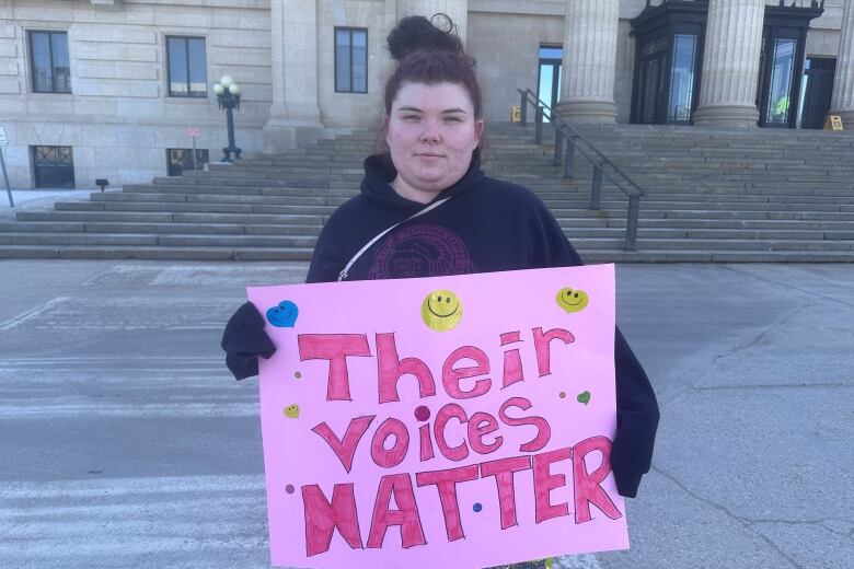 A woman with red hair in a pony tail holds a sign that says, 