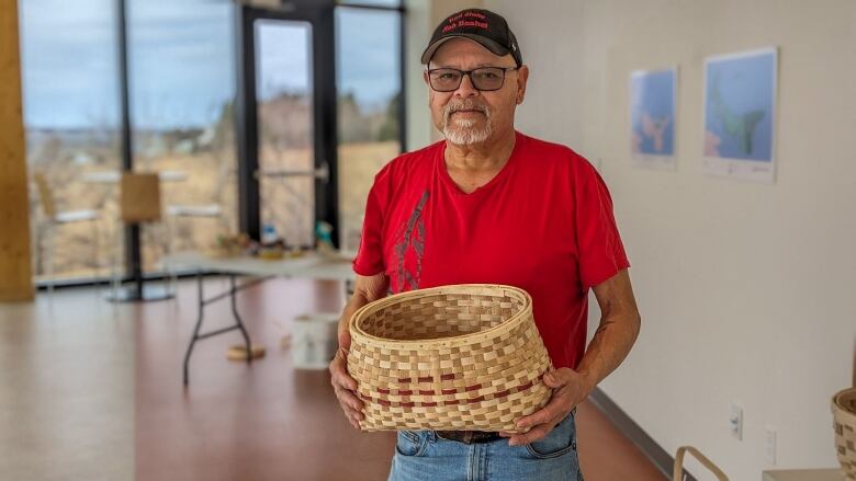 A man in a red Tshirt holds a handmade basket 