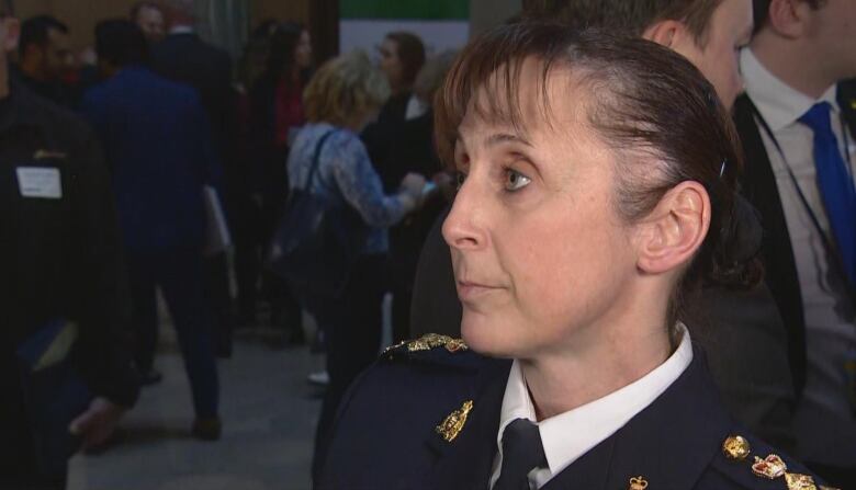 a woman with her hair in a bun wearing an official uniform backgrounded by a crowded room