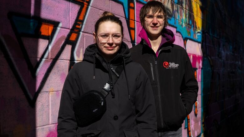 Two women stand in front of a graffitti wall.