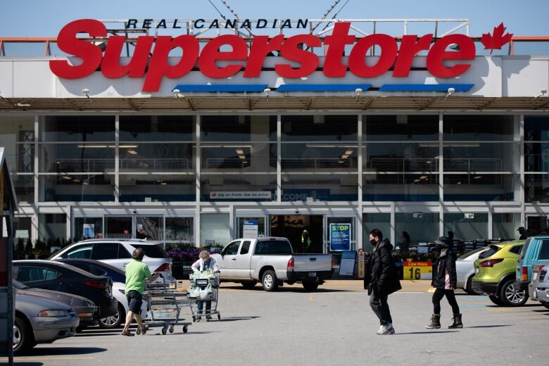 A large supermarket parking lot, with vehicles and people milling about, is pictured.