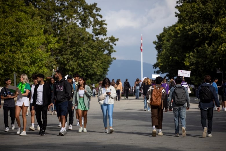 Groups of students mill around on a path leading to a Canada flag at a university campus.