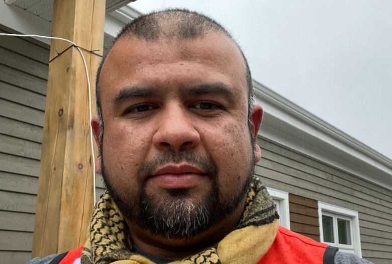 A man with a beard wearing a scarf stands in front of a building.