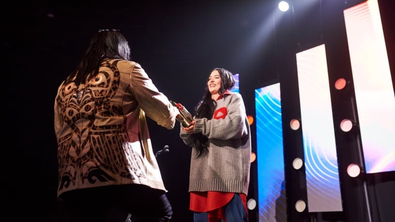 Artist Aysanabee walks up onstage to accept his Juno Award from singer-songwriter Lauren Spencer Smith.