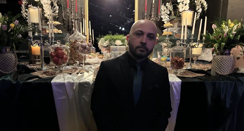 A man wearing a black suit sits in front of a table full of food.