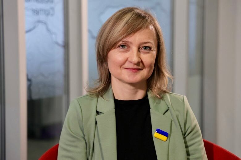 A woman in a green suit wears a pin of the Ukrainian flag on her lapel.