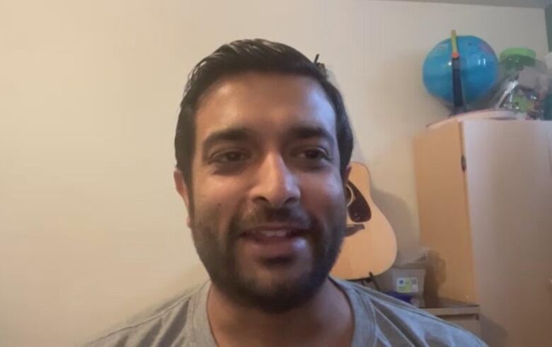 A South Asian man smiles while seated in front of a guitar.