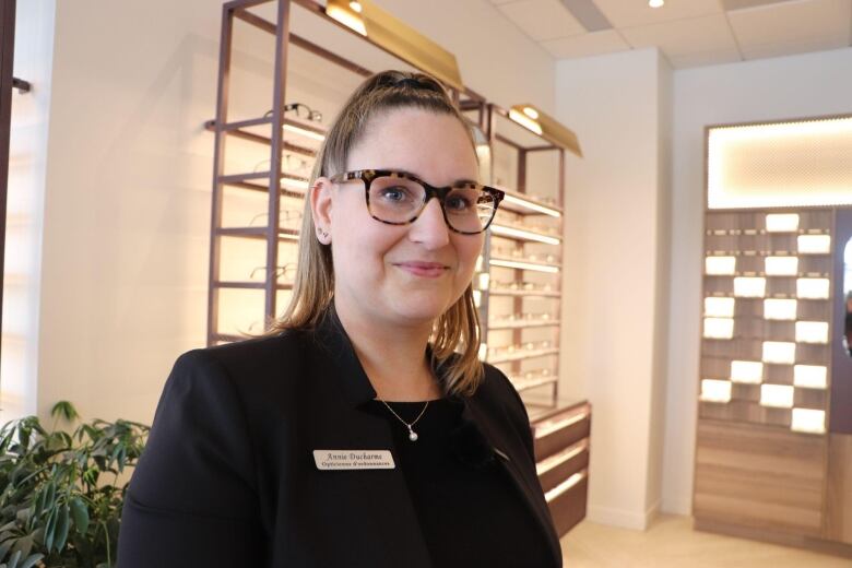 A woman smiles at the camera. Behind her is a display of glasses.