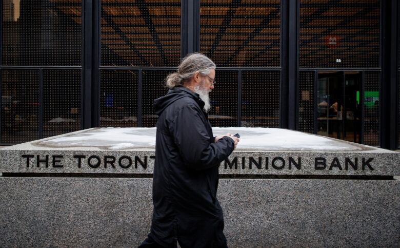 A man walks past a sign that says 'The Toronto Dominion Bank.