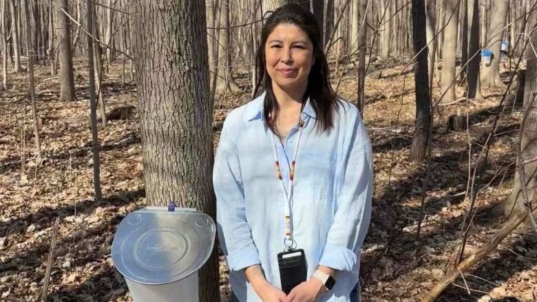 A woman stands beside a tree with a maple sap tap.