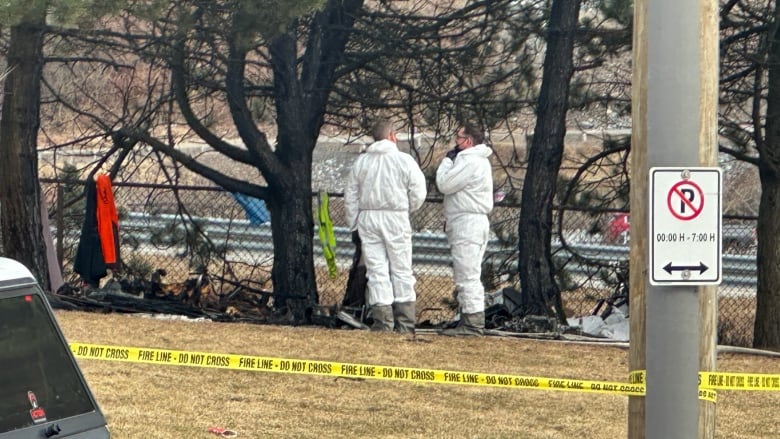 Two men in hazmat suits stand in a wooded grassy area. 