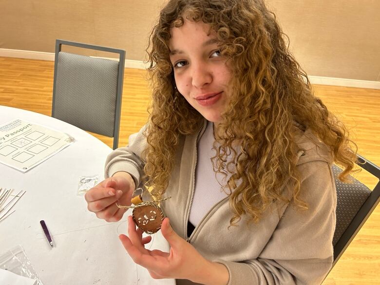 a girl holding a circular piece of birchbark with quillwork designs on it.