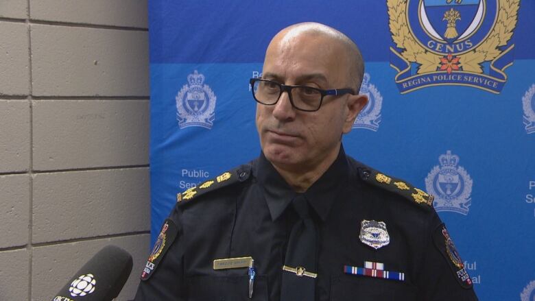 Man wearing glasses with a bald head stands in front of a podium to speak to reports.