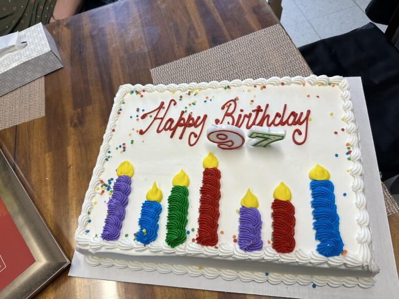 A white, rectangular cake with colourful candles made of frosting reads Happy Birthday.