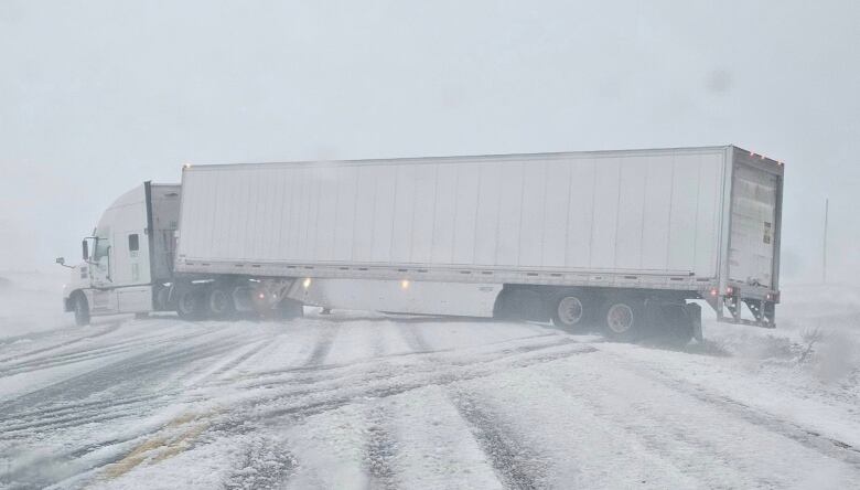 A tractor trailer across a highway in snowy conditions.