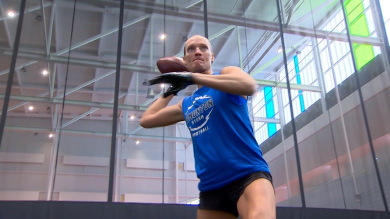 A woman wearing black shorts and a blue shirt holds a football in the air.