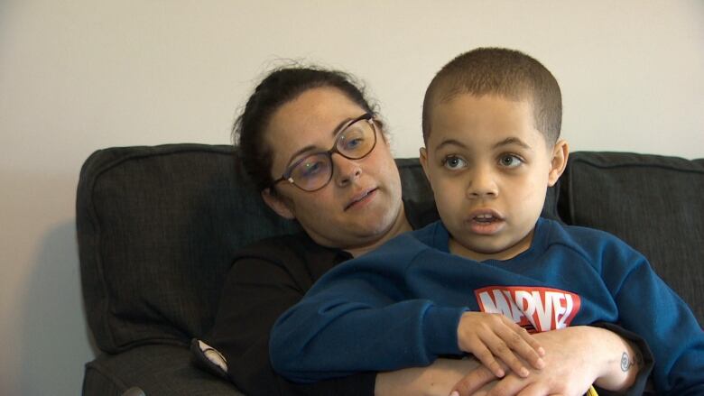 A woman with brown hair and glasses holds her eight-year-old son. He's wearing a long-sleeve Marvel tee-shirt. 