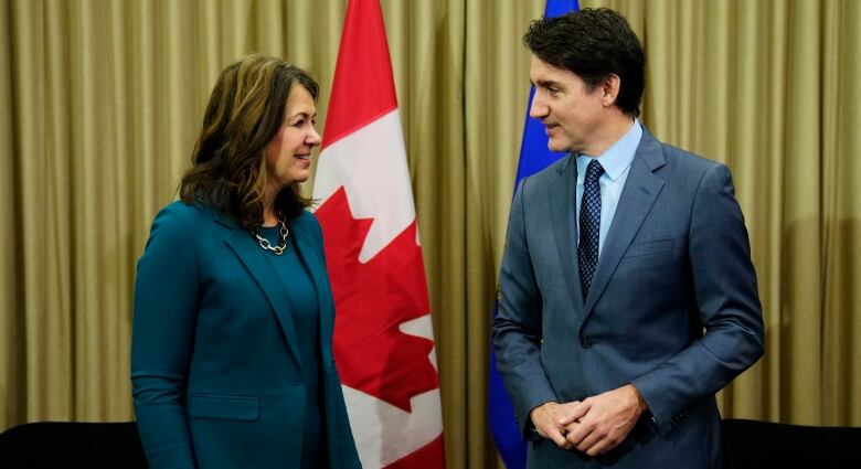 A woman with medium-length brown hair and a teal-coloured suit smiles as a tall brunette man wearing a blue suit.