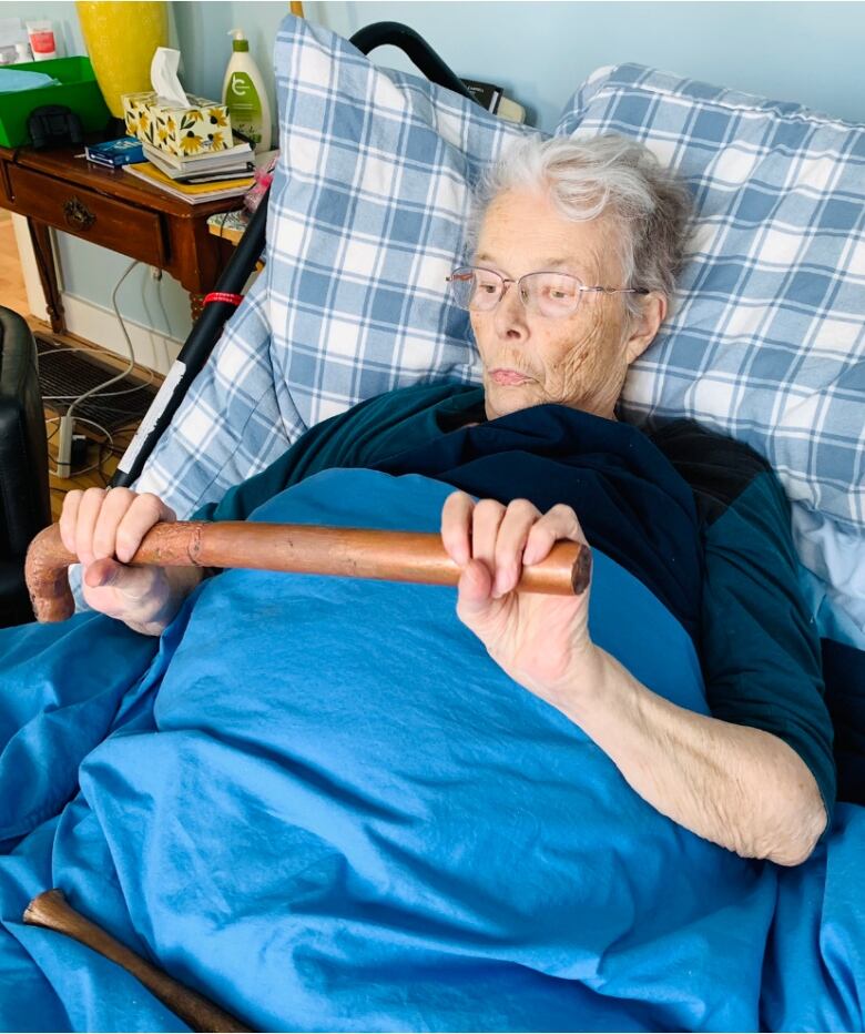 An elderly woman in a hospital bed examines a long tube-like artifact. 