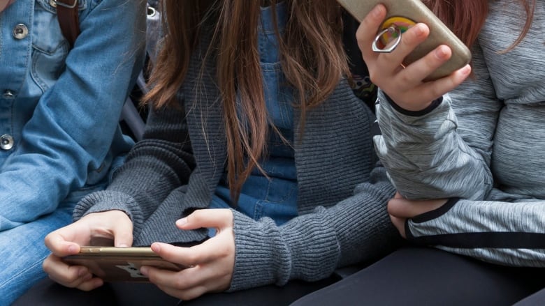 Two young teenage girls sitting holding smartphones in their hands. 