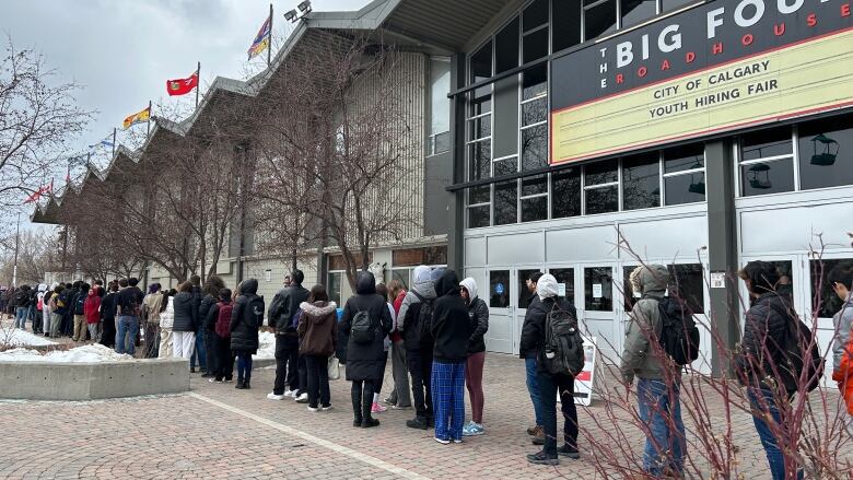 a long lineup of young people pictured standing outside a building.