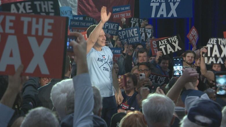 A man in a light blue shirt waves, while a throng of people around him celebrate and wave signs in the air. 