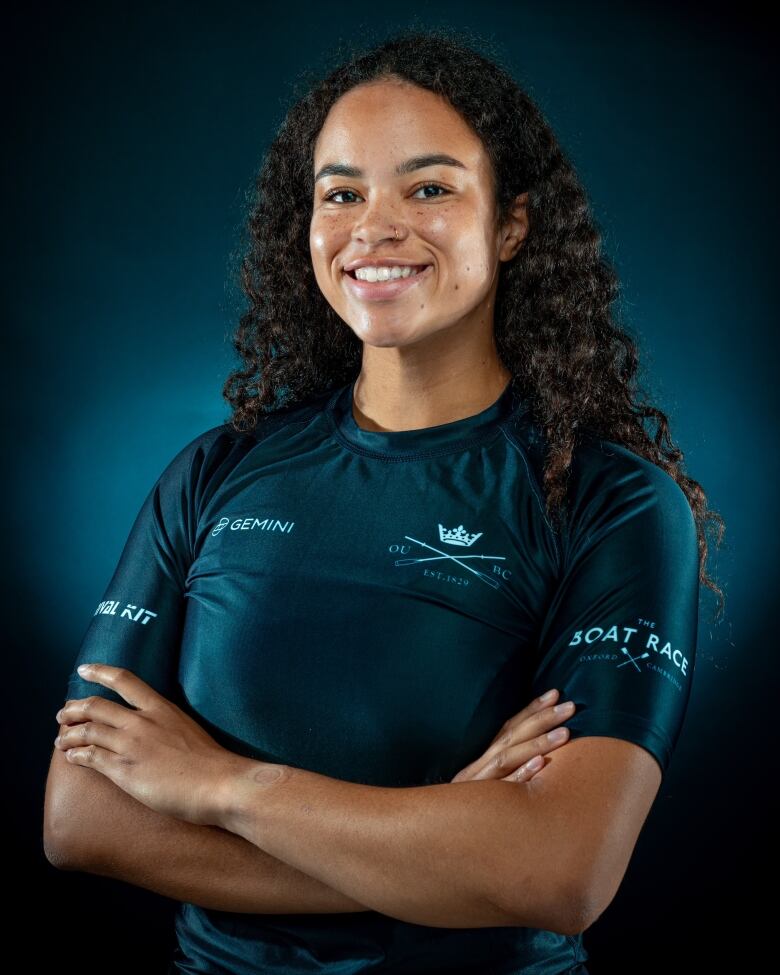 A woman in a rowing jersey with long curly hair and her arms crossed poses for a headshot.