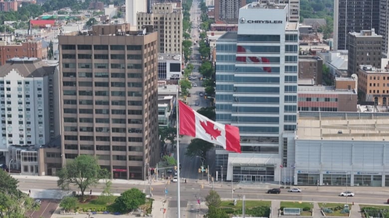 A Canadian flag flies in front of skyscrapers.