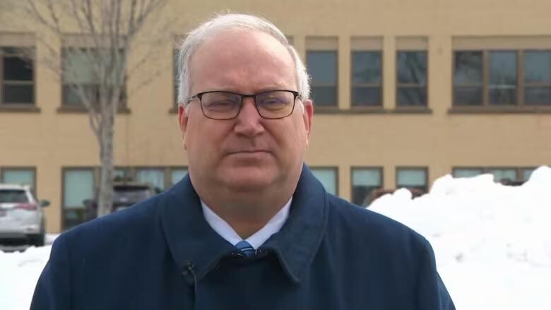 A white man with white hear wearing black glasses and a blue coat.