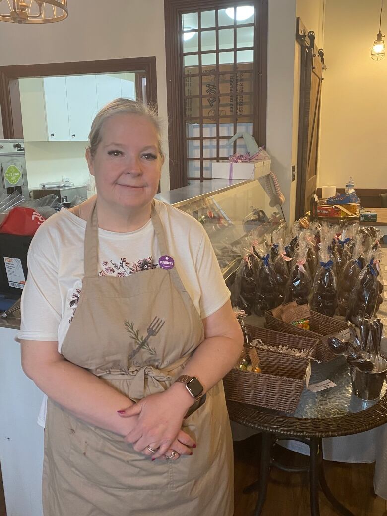 A woman in a tan apron stands in front of a counter full of chocolate Easter bunnies.