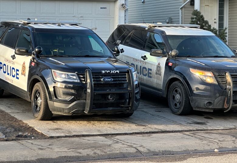 Two marked police cruisers backed into a driveway in front of a home.