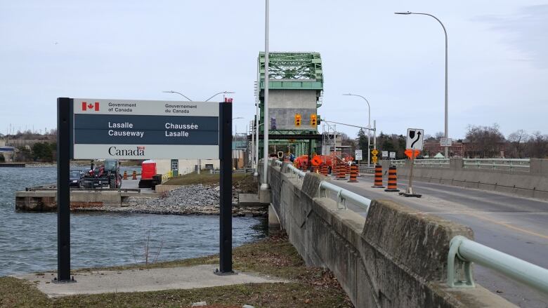 A green bridge can be seen behind a row of orange pylons. A sign identifies the crossing as the LaSalle Causeway.