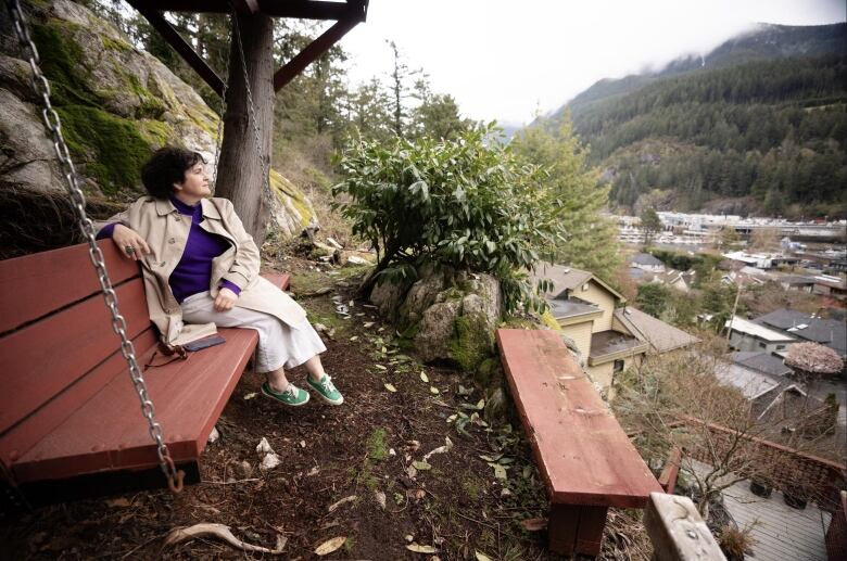 A woman sits on a swing overlooking a village. 