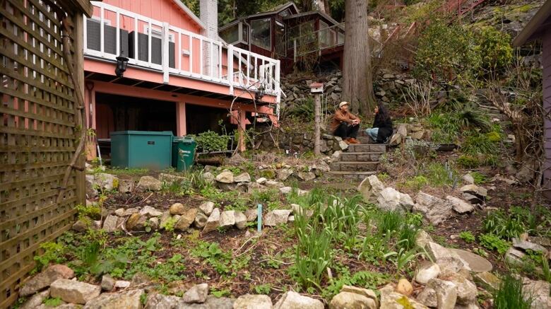 A man and a woman sit on a steps between cottages.