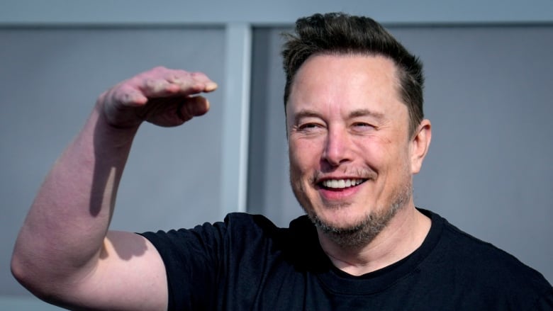 A man in a black t-shirt smiles and waves.