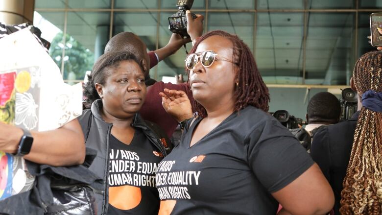 Two women stand next to each other among a crowd of people. They are wearing matching shirts that say:  