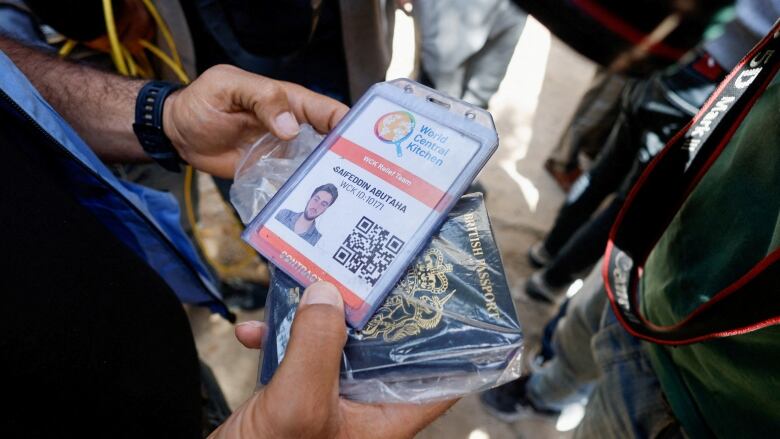 A person holds a document of an aid worker named Saifeddin Issam Ayad Abutaha. A British passport is also visible.